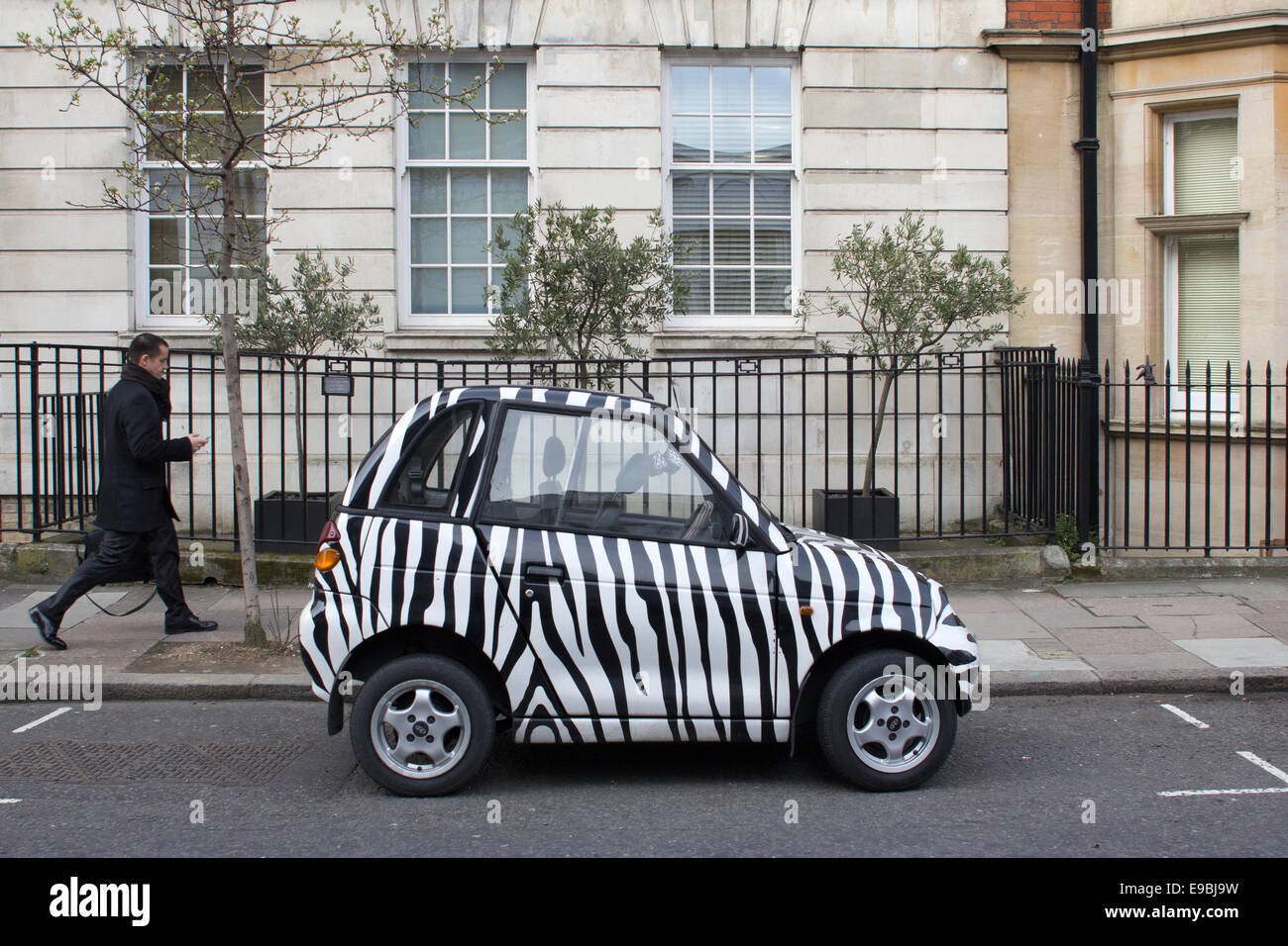 ein-kleines-auto-lackiert-in-zebra-farben-mit-einem-mann-zu-fuss-auf-einer-londoner-strasse-ge...jpg